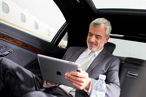 Ein Fahrgast sitzt in einer Limousine mit einem Tablet in der Hand.