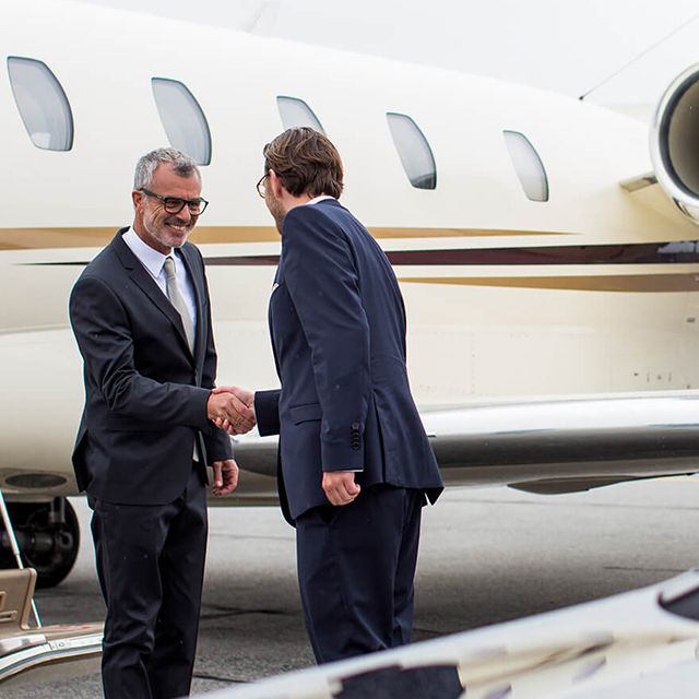 Ein Chauffeur schüttelt einem Fahrgast die Hand vor einem Business-Jet.
